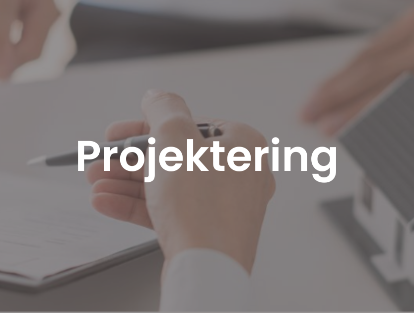 En bild på en hand som håller i en penna med ett miniatyrhus till höger på bordet. 